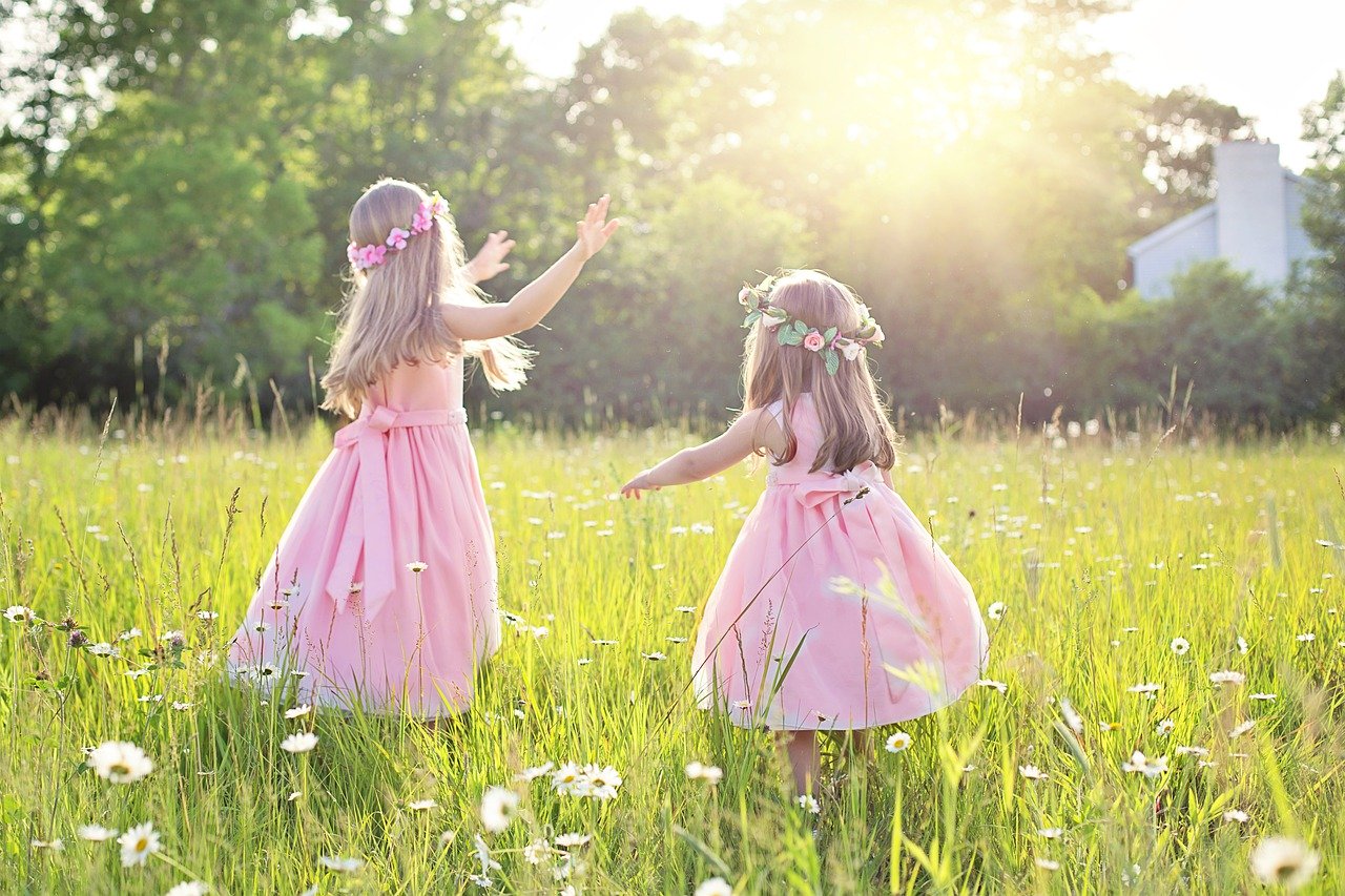 two young girls wearing preppy pink dresses playing in a field