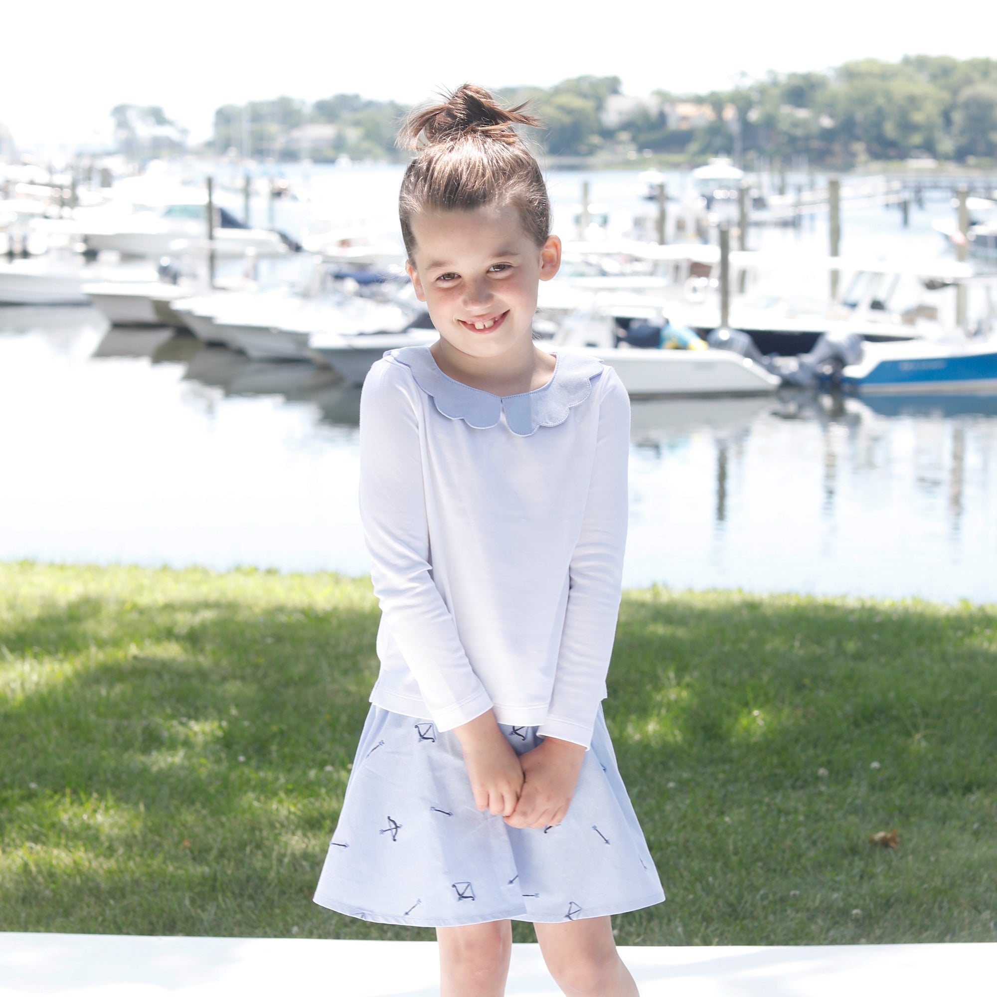 image of a young girl wearing a preppy bow and arrow oxford skirt and peter pan collar shirt in front of a boat marina