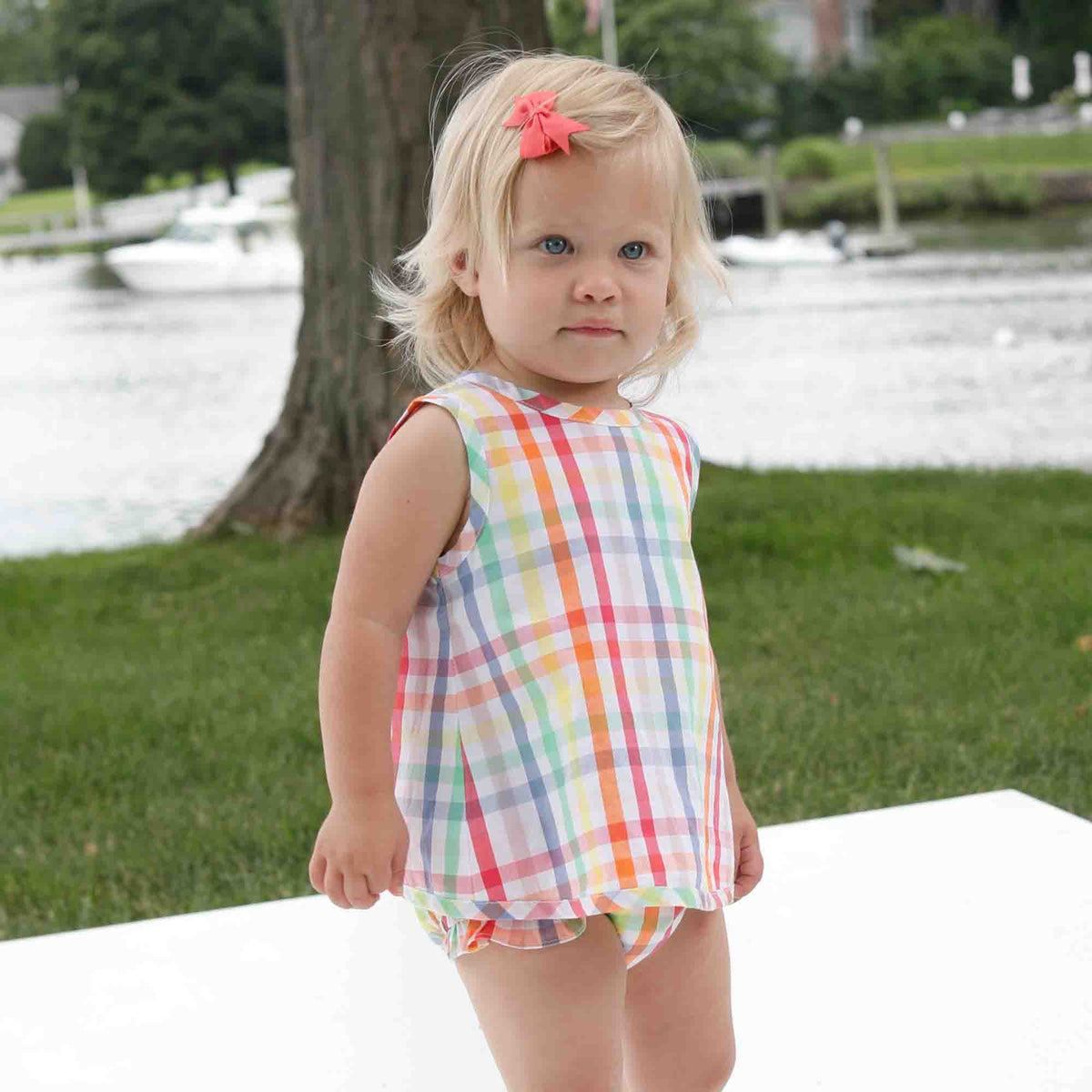 adorable baby girl wearing a preppy rainbow gingham sunsuit at the park 